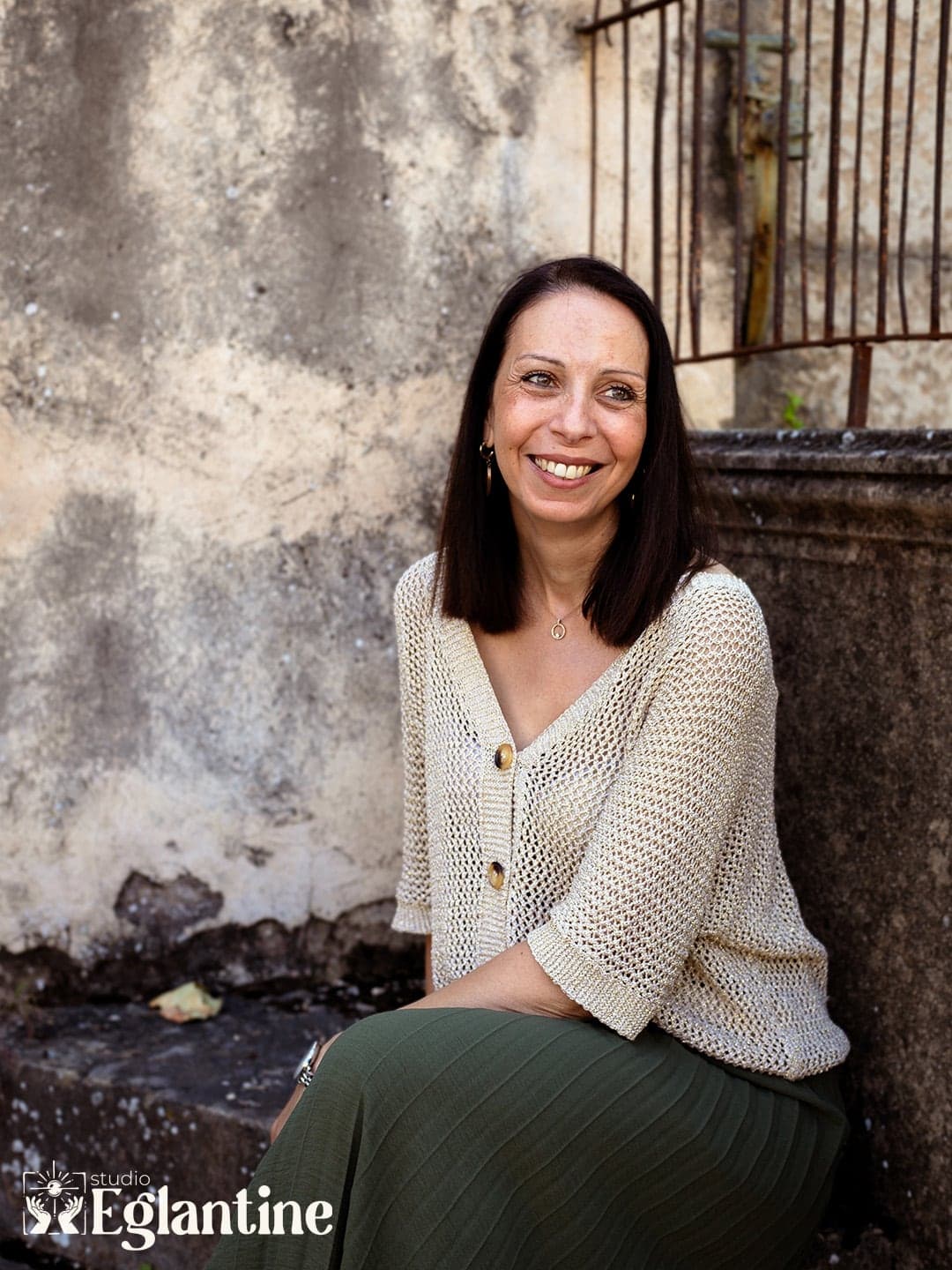 Christèle Cattier, souriante, assise devant un mur ancien